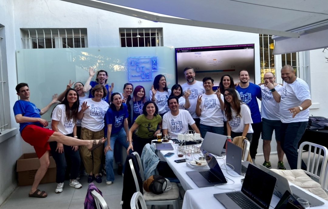 Foto grupal del equipo de Decide Chile con poleras blancas y azules de Decide Chile bajo el letrero de neón.