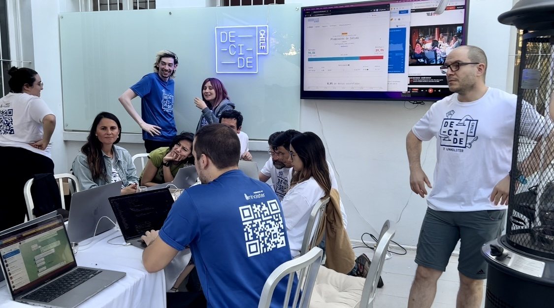 Equipo trabajando en notebooks; una polera azul lleva un código QR a la plataforma en la espalda.