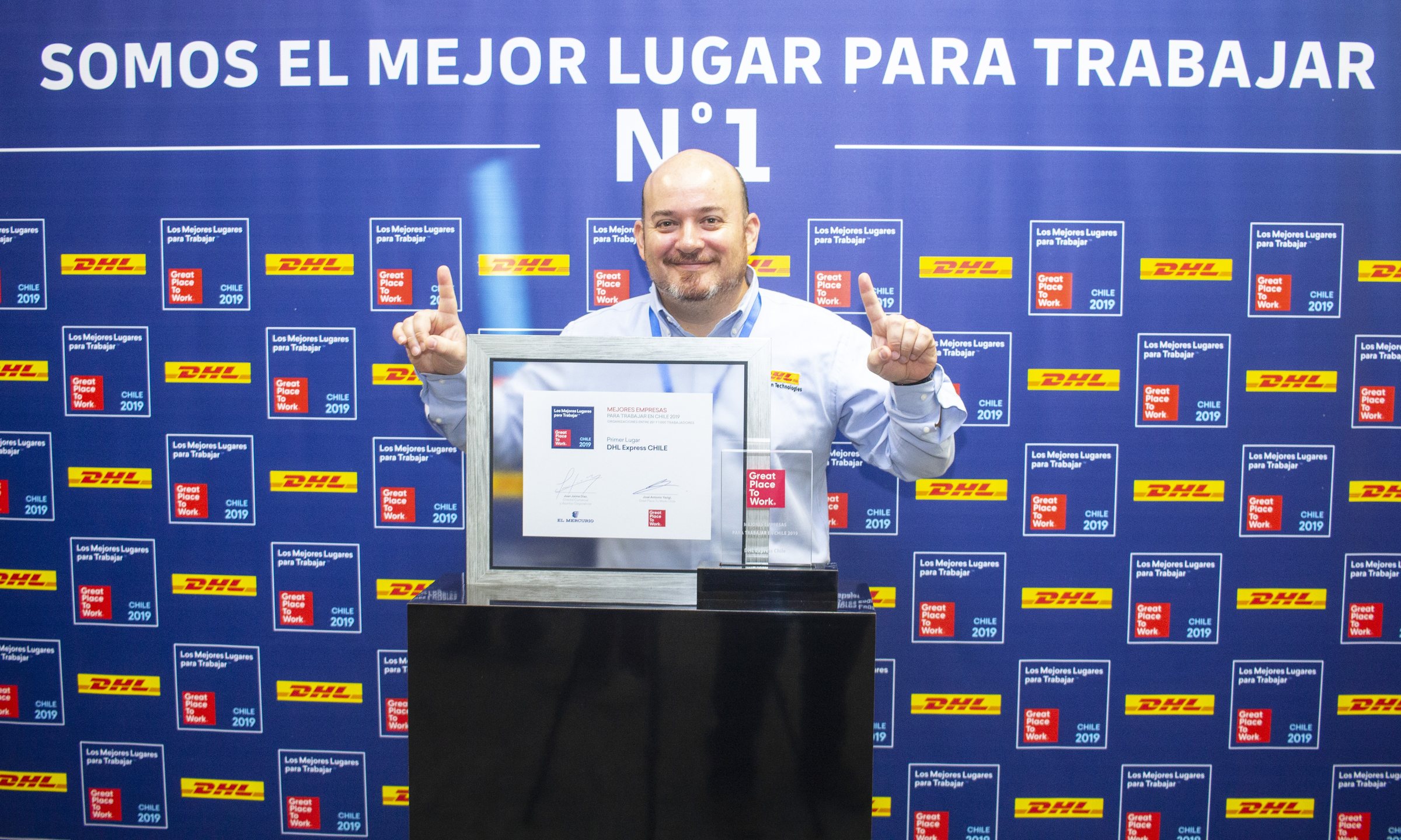 Un colaborador de DHL posa con su diploma frente al fondo fotográfico de Great Place to Work 2019.