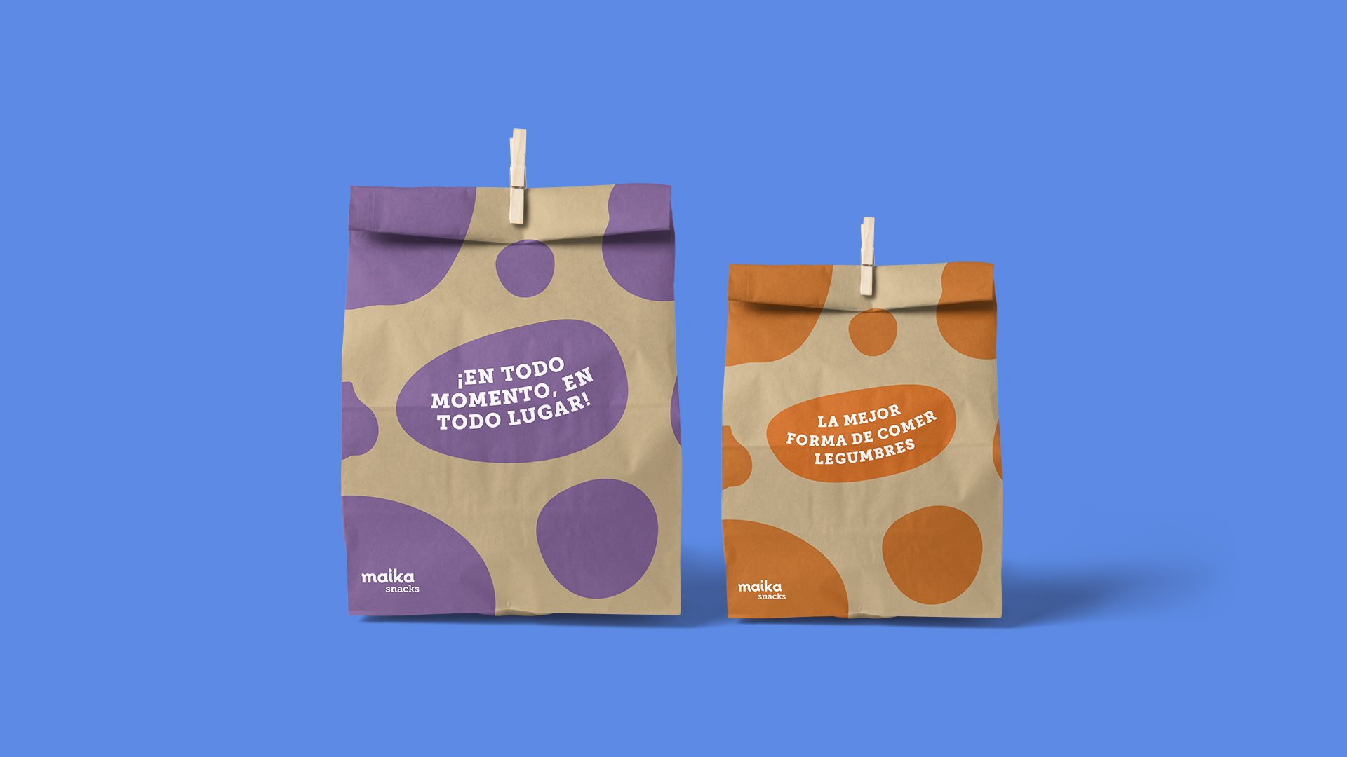 Dos bolsas de papel kraft de Maika con manchas violeta y naranja sobre fondo azul.