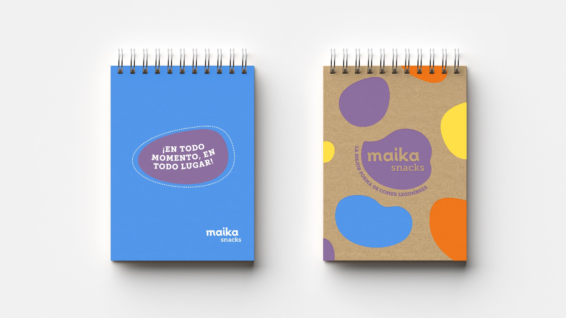 Diseño de dos libretas anilladas de Maika: tapa azul con «¡En todo momento, en todo lugar!» y tapa kraft con manchas de colores y el isologo.