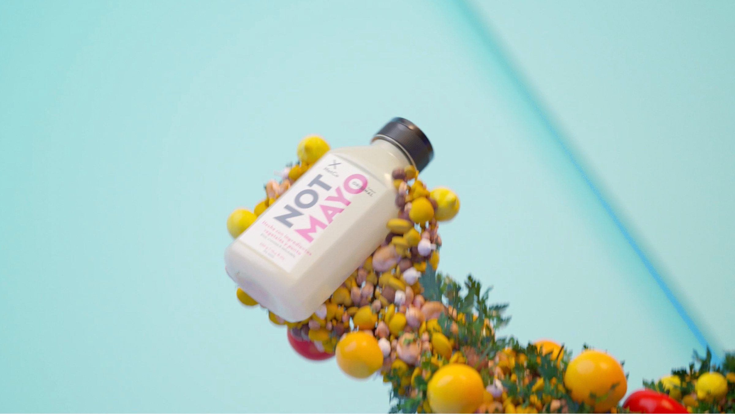 Cuadro del video: una botella de NotMayo cae entre tomates, limones y hojas.