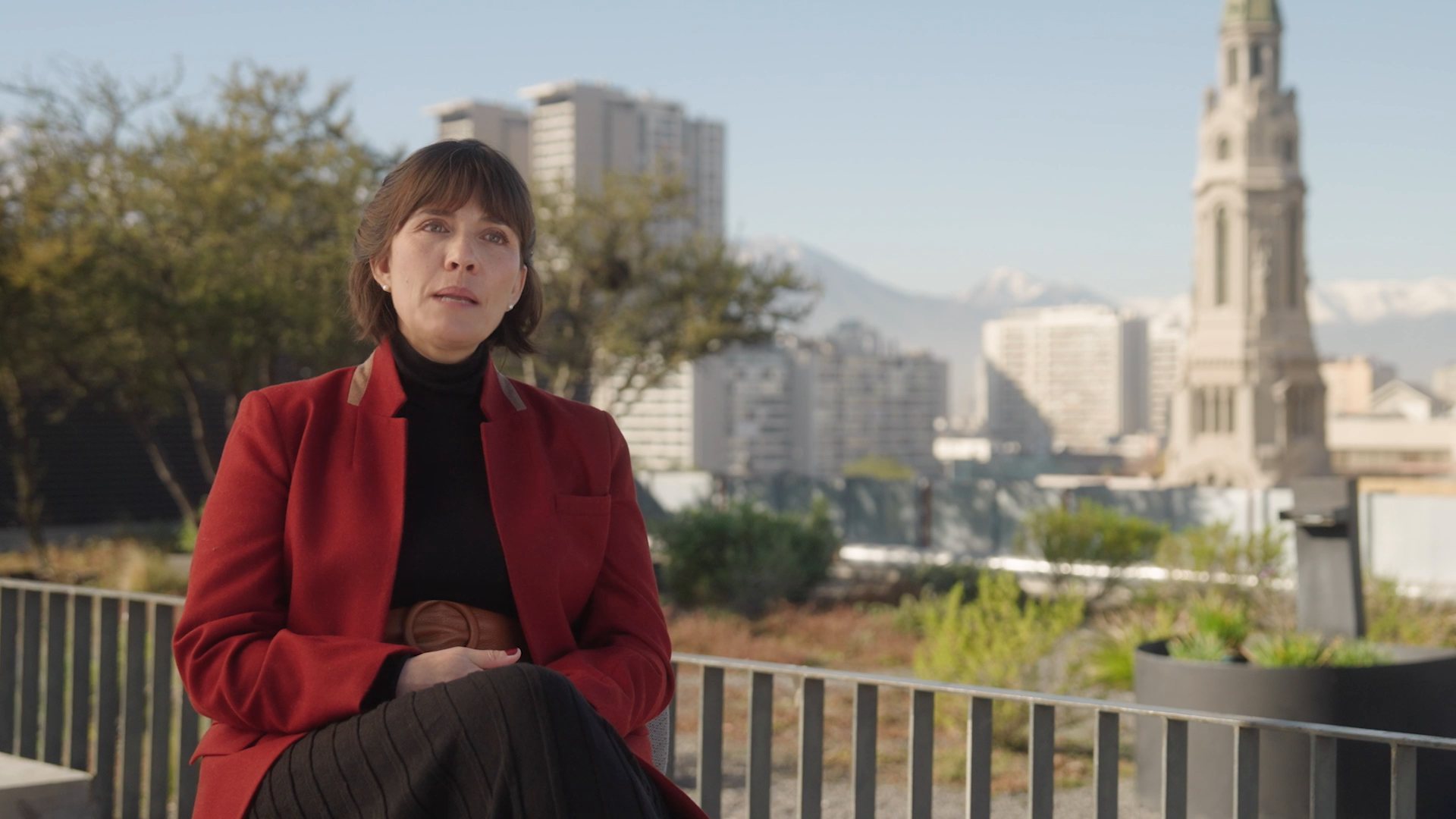 Carolina Busco entrevistada en una terraza, con la ciudad y la cordillera de fondo.