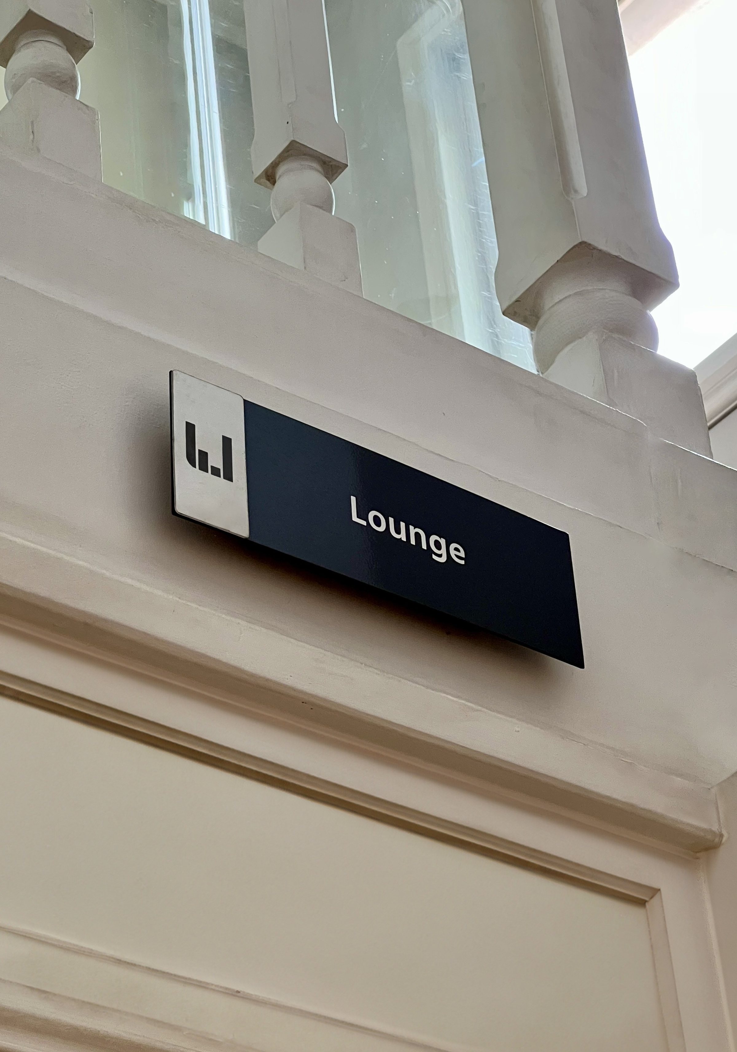 Señalética de sala «Lounge» con el isotipo, sobre el marco de una puerta.